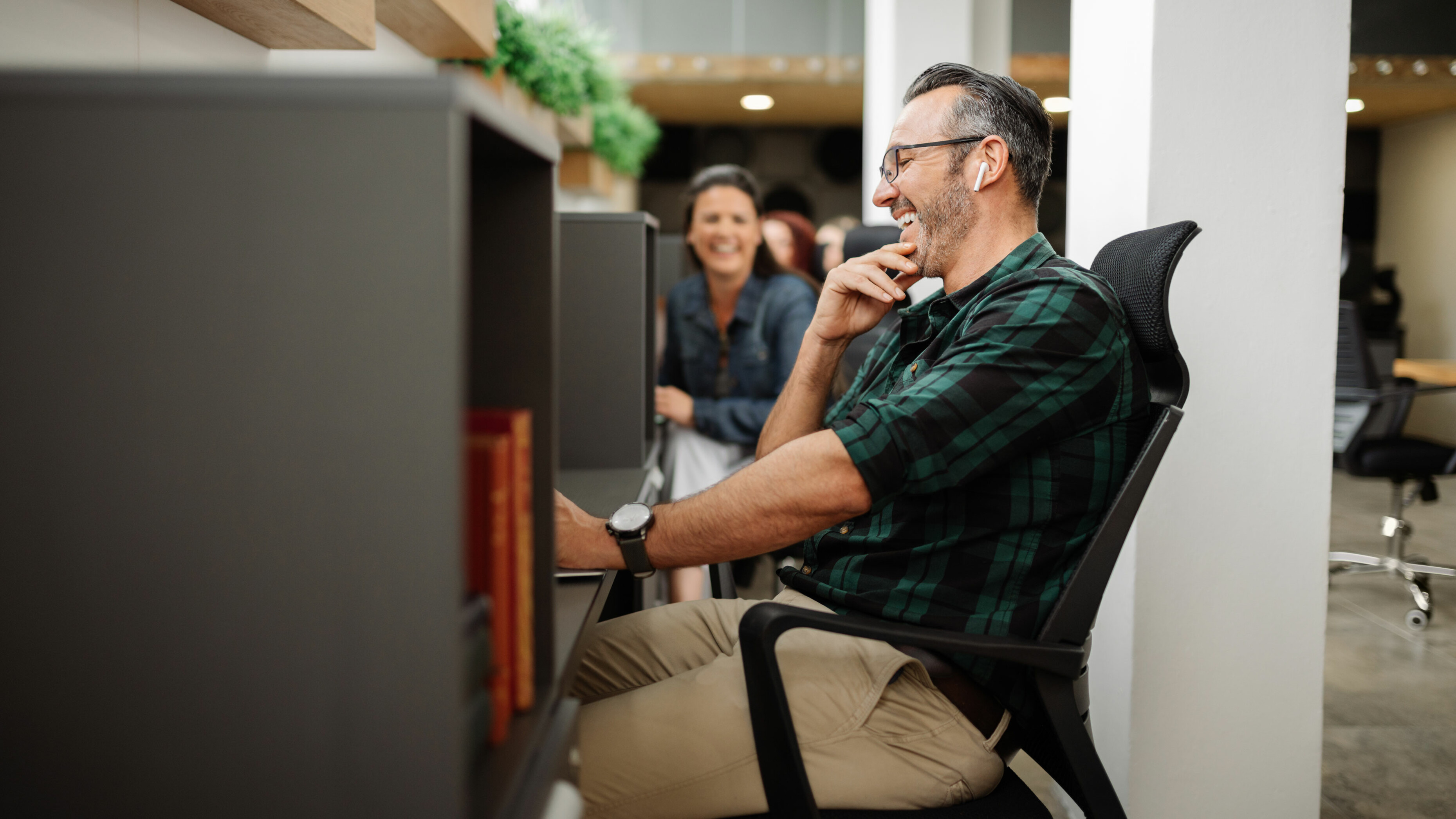 Man sitting at a cubical desk smiling and laughing as coworker next to him smiles